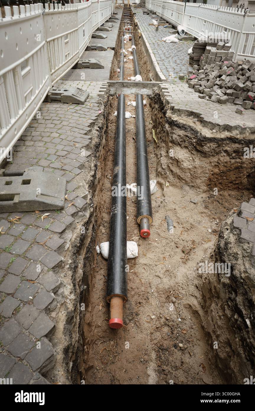 Una lunga e stretta trincea è scavata lungo una strada per posare tubi di teleriscaldamento Foto Stock