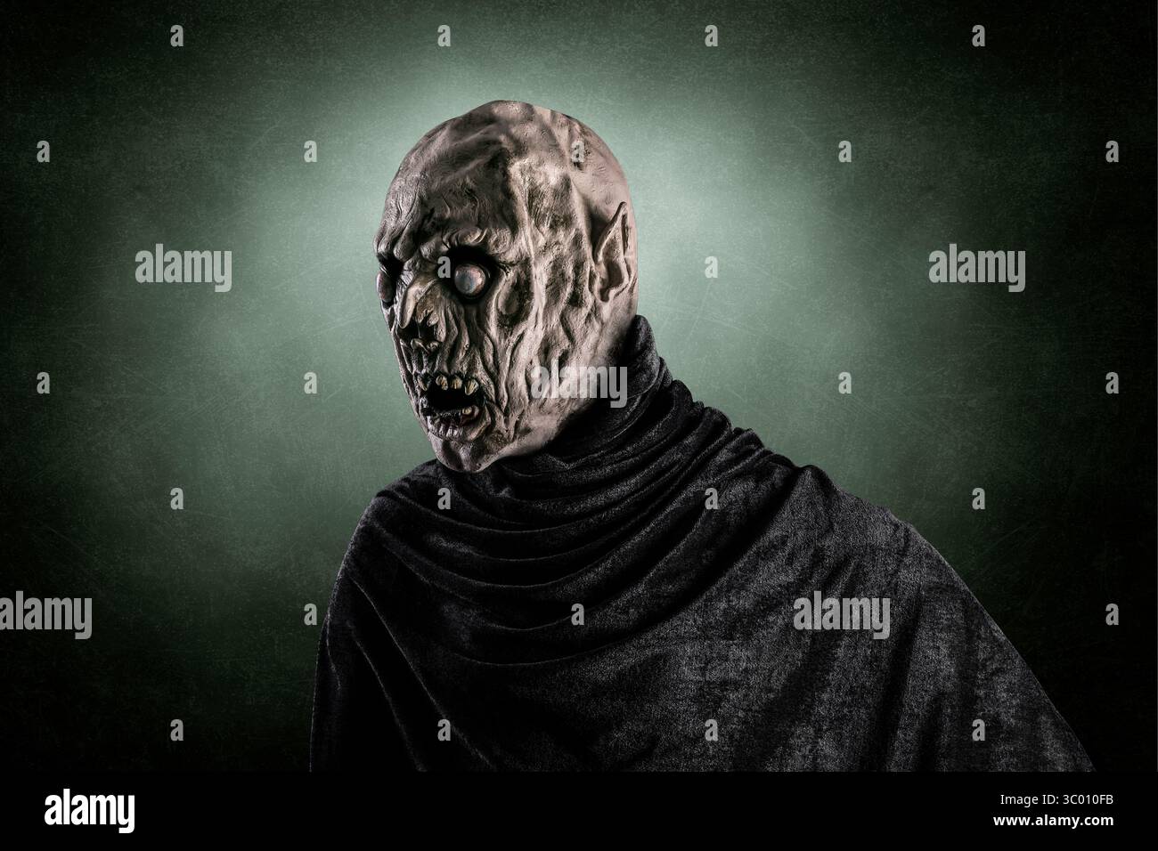 Ritratto di uno zombie con mantello con cappuccio su sfondo verde scuro e nebbioso Foto Stock