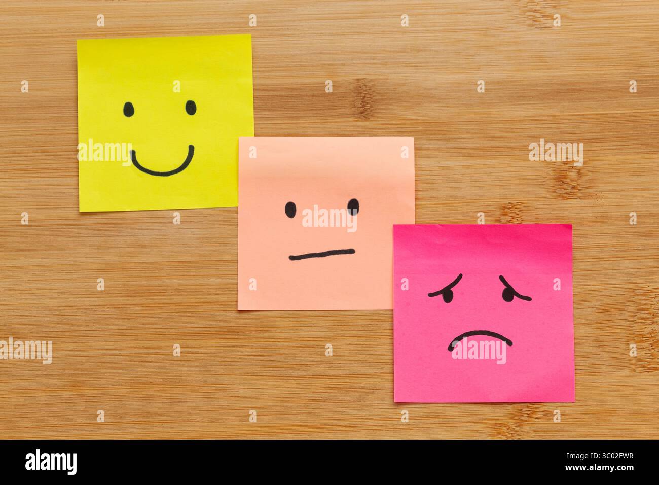 Primo piano di tre note appiccicose con rappresentazioni di emozioni umane su sfondo di legno Foto Stock