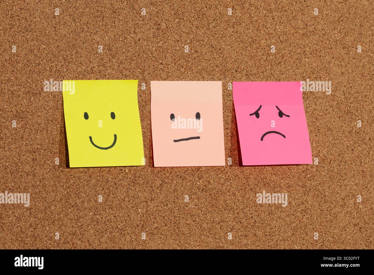 Primo piano di tre appiccicose note con emozioni umane raffigurazioni di volti su uno sfondo in sughero Foto Stock