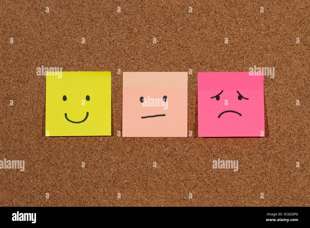 Primo piano di tre appiccicose note con emozioni umane raffigurazioni di volti su uno sfondo in sughero Foto Stock