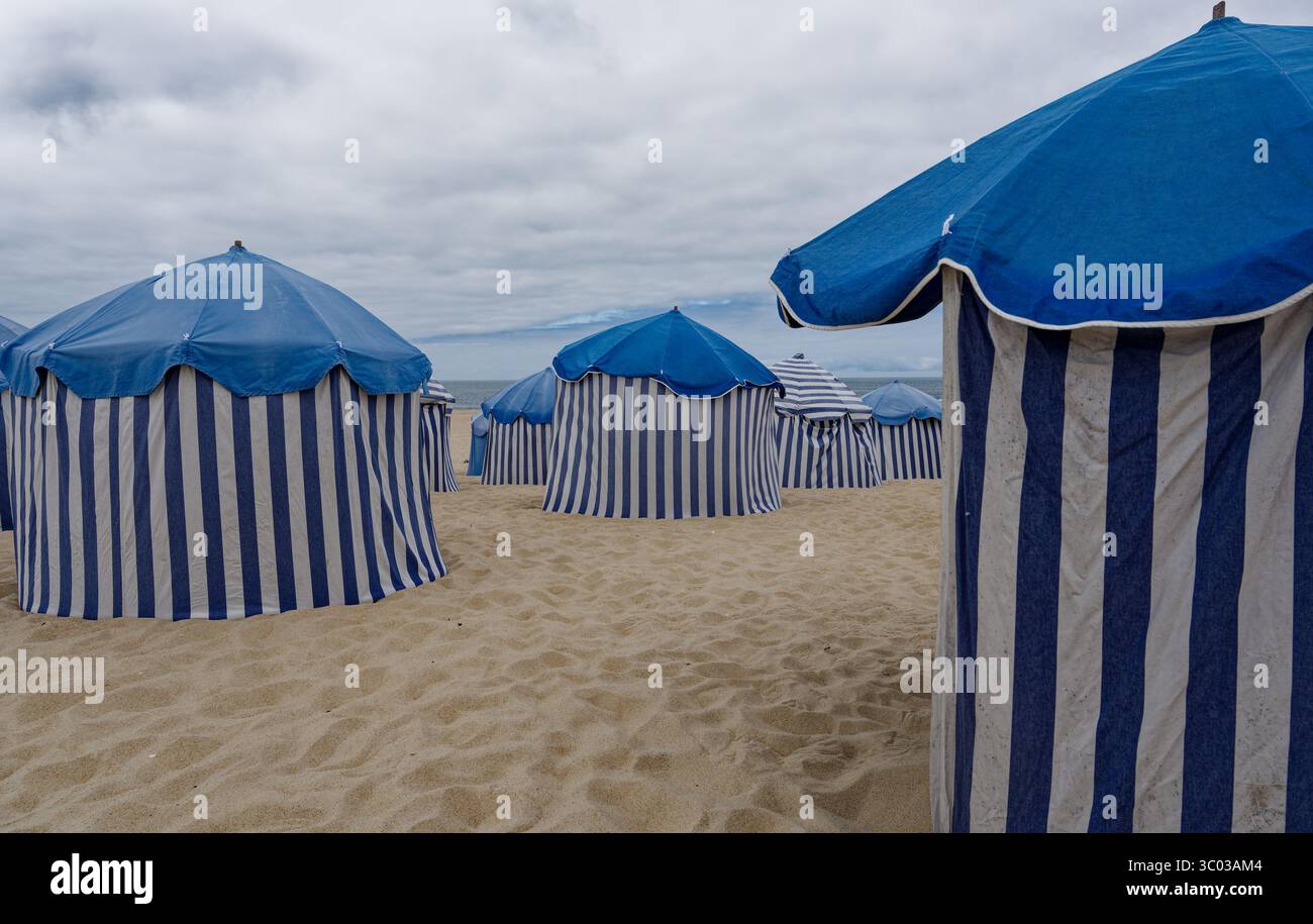 Iconiche tende da spiaggia a righe blu e bianche sulle rive sabbiose di Figueira da Foz sotto un cielo estivo mostruoso Foto Stock