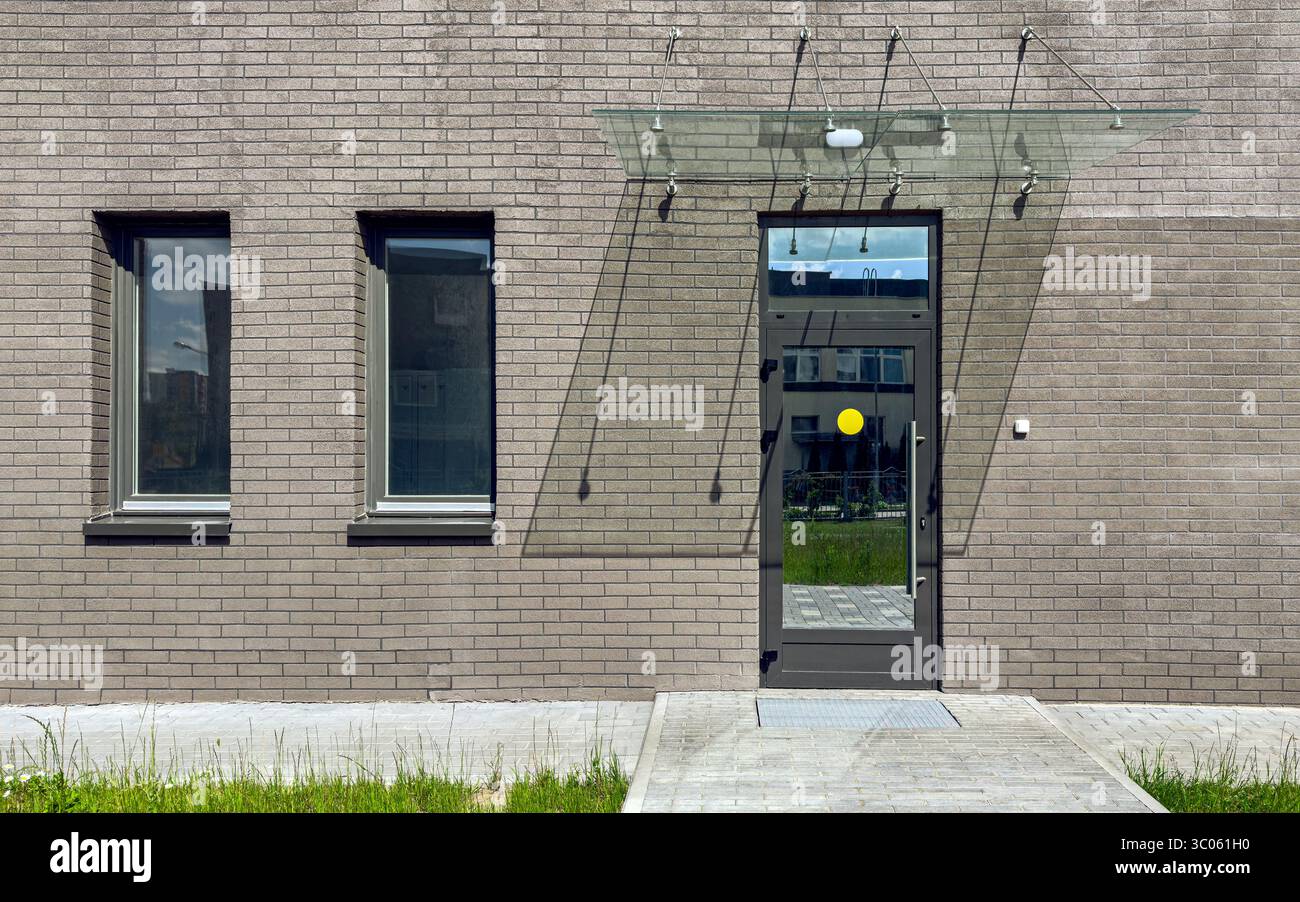 facciata di un moderno edificio di appartamenti. sfondo murato grigio con porta e due finestre. Foto Stock