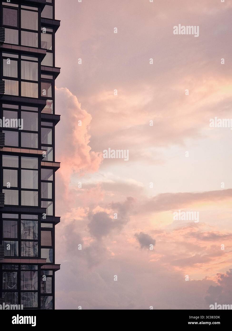 Parte di un edificio residenziale che si affaccia sul suggestivo cielo del tramonto. Alto edificio moderno e nuvole color pesca sullo sfondo. Foto Stock