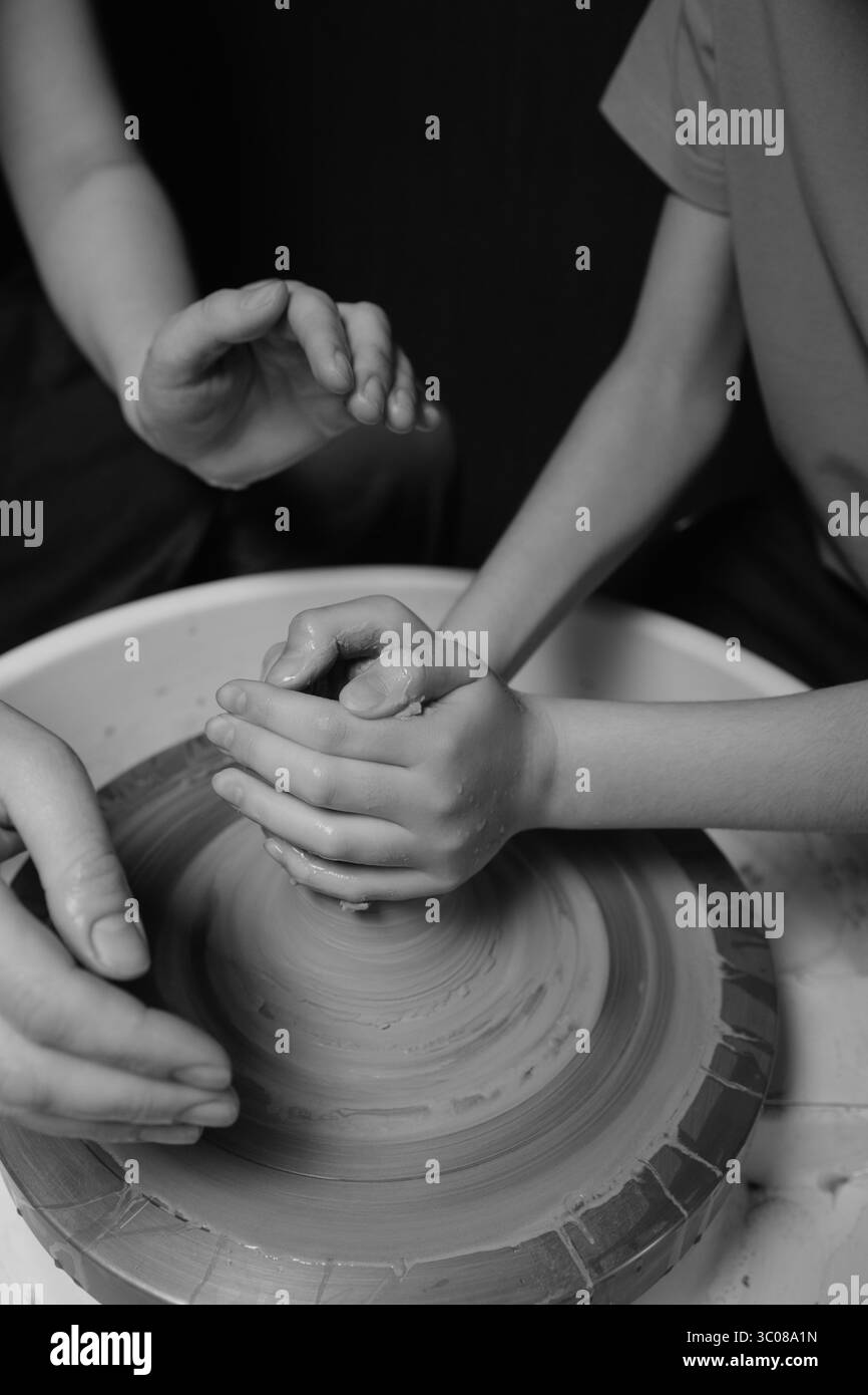 Madre e figlio realizzano ceramiche su ruote nello studio di ceramica con mani coperte di argilla Foto Stock
