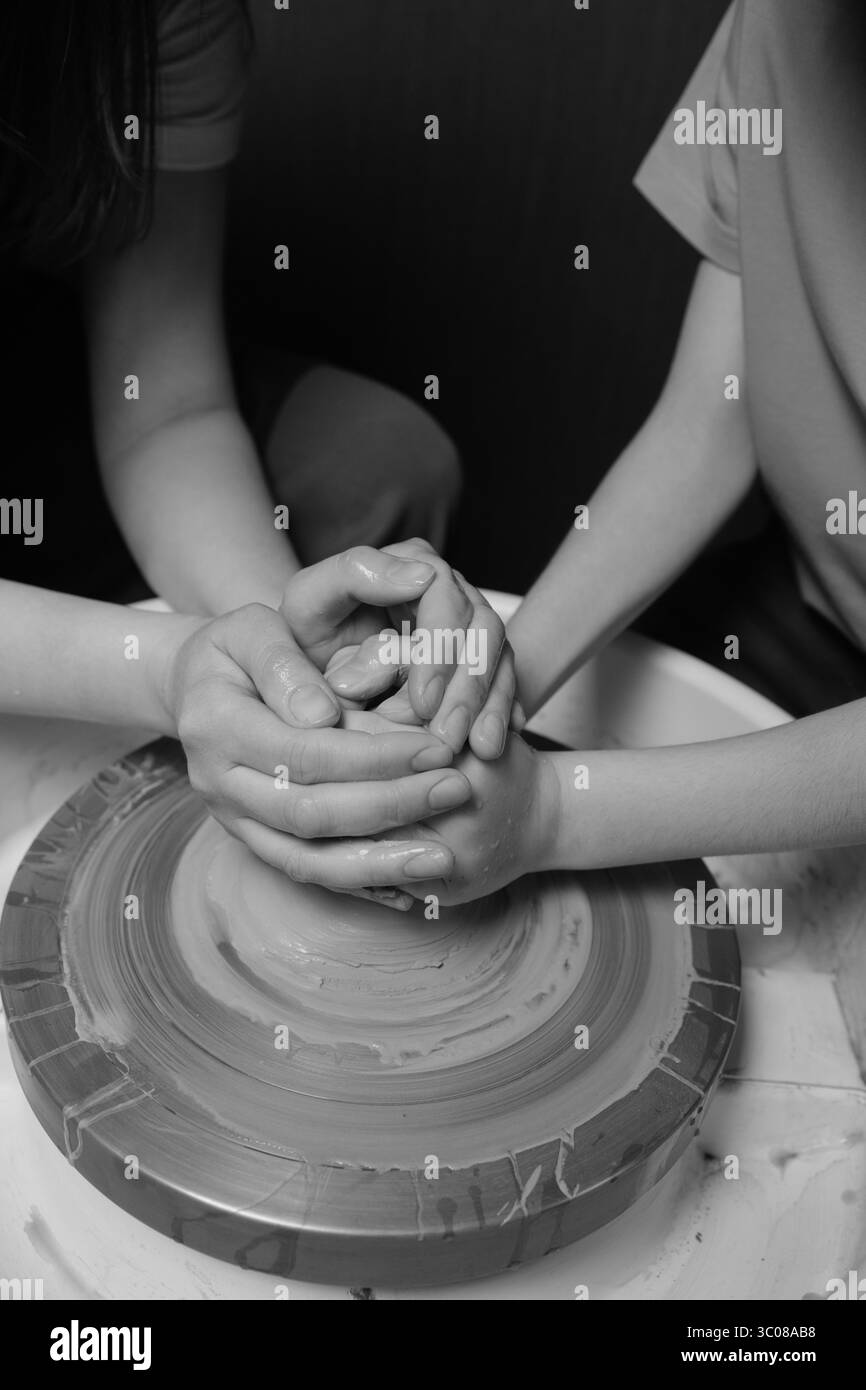 Madre e figlio realizzano ceramiche su ruote nello studio di ceramica con mani coperte di argilla Foto Stock
