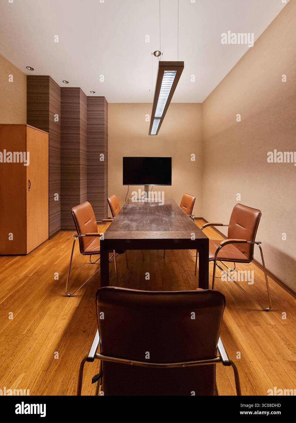 Il capo del tavolo è seduto nella sala riunioni in toni caldi. Vista simmetrica di una moderna sala conferenze con pareti beige, sedie abbronzanti e tavolo marrone Foto Stock