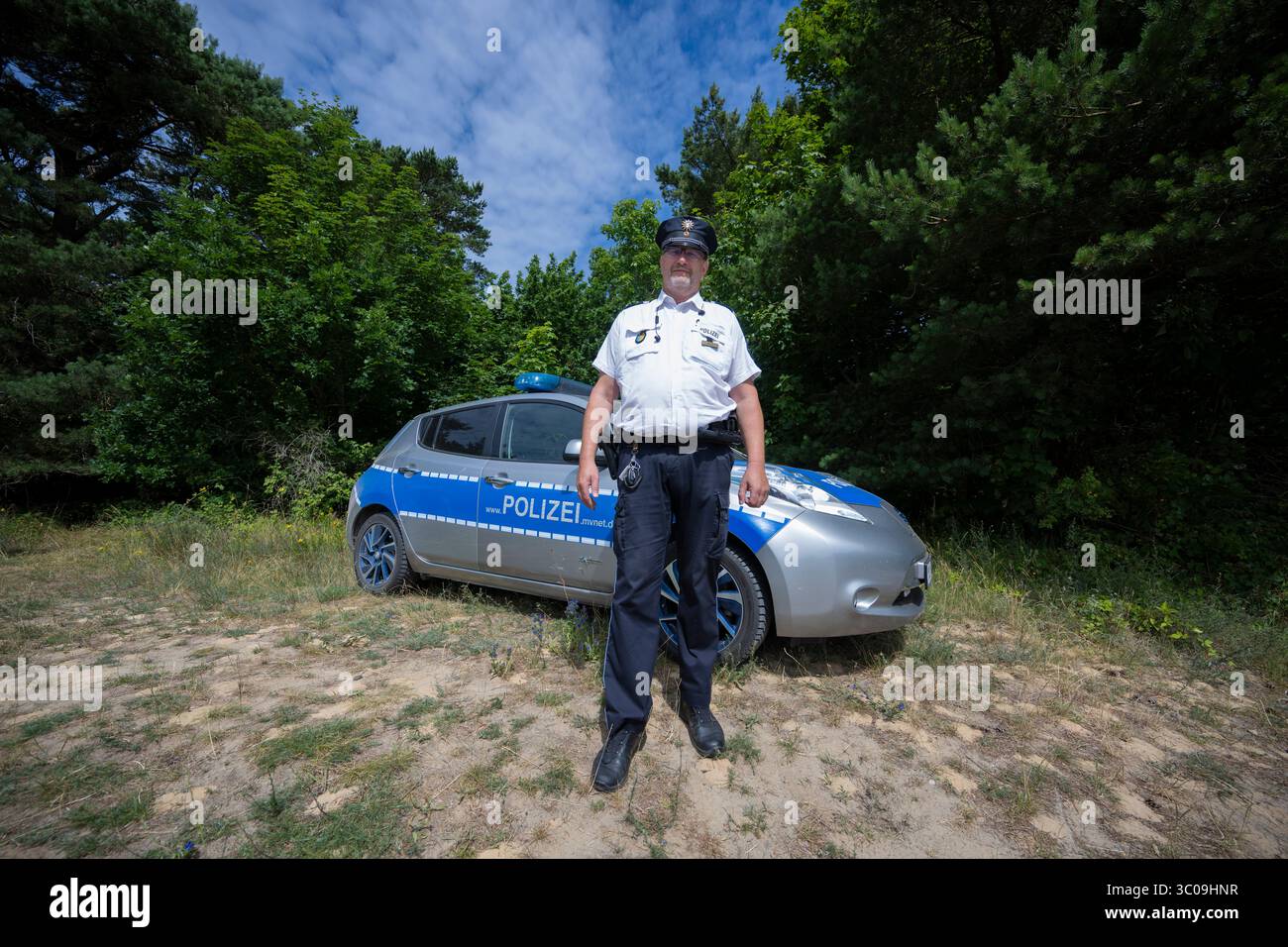 Hiddensee, Germania. 10 luglio 2025. Il capo agente Thomas Moritz si trova di fronte a un'auto della polizia. Per la maggior parte dell'anno, l'agente di contatto Thomas Moritz è l'unico agente di polizia sull'isola di Hiddensee sul Mar Baltico. Crediti: Philip Dulian/dpa/Alamy Live News Foto Stock