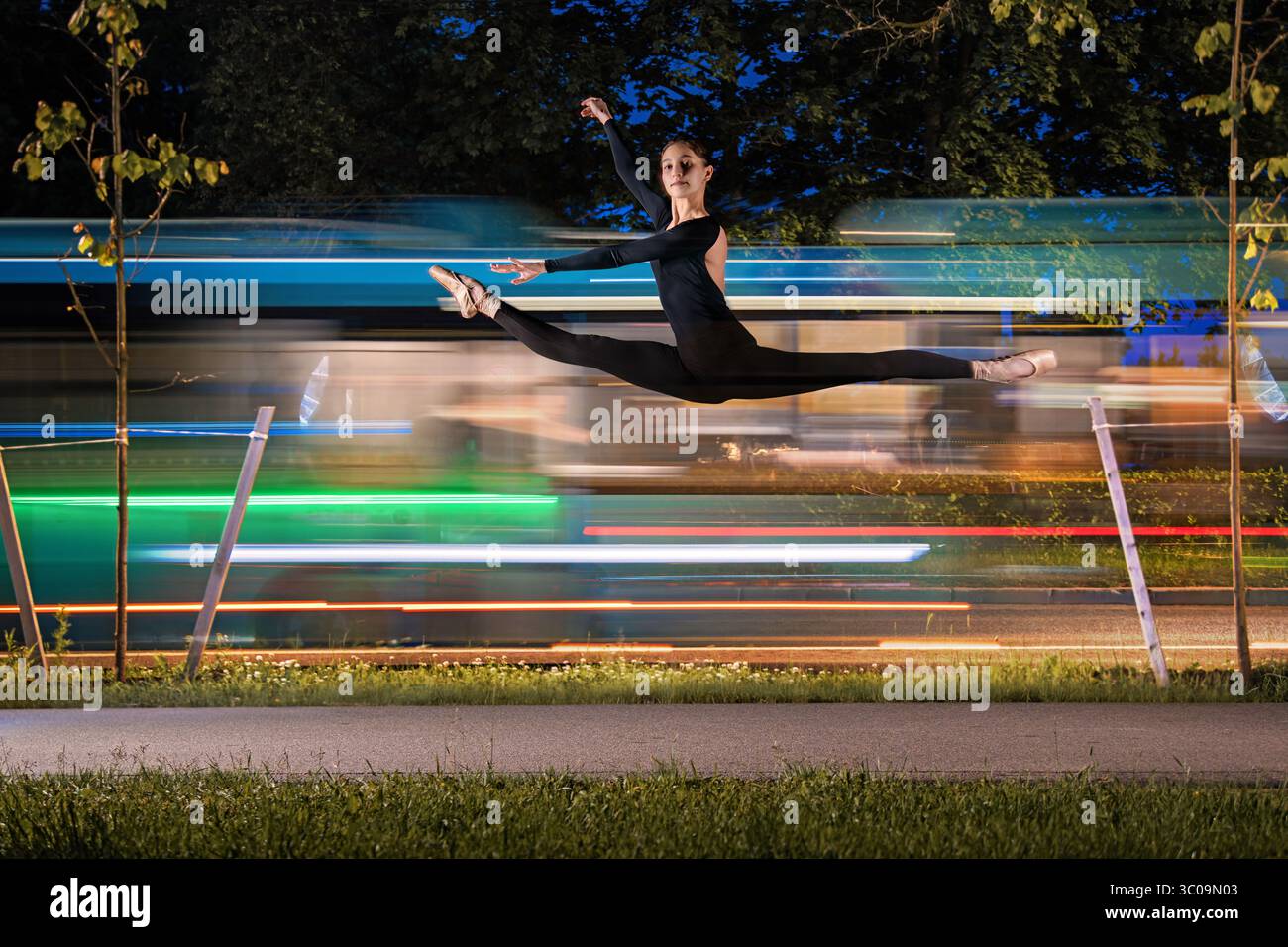 Ballerina che salta sullo sfondo di sentieri leggeri dalle auto di notte. Foto Stock