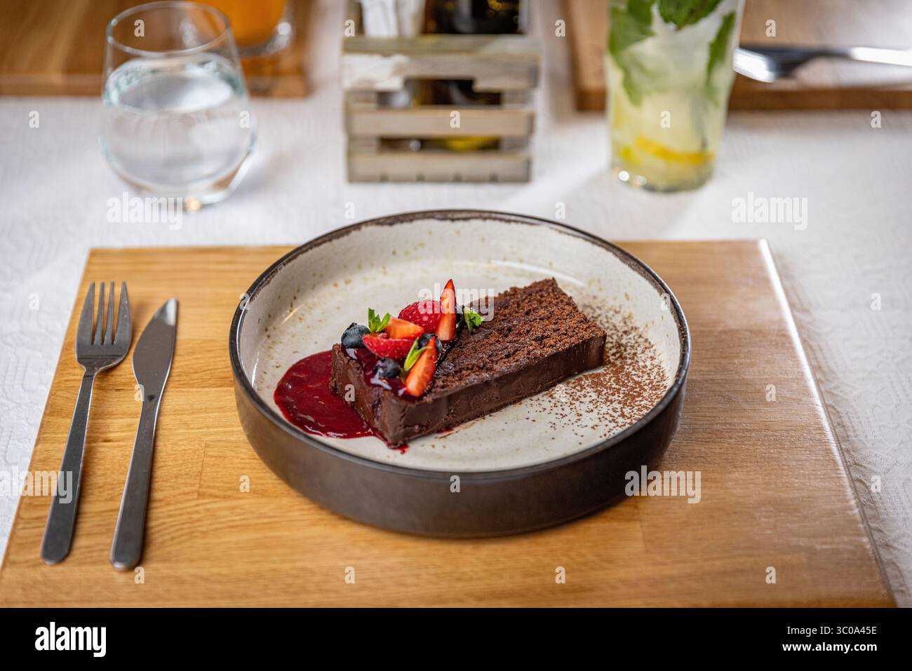 Deliziosa torta al cioccolato guarnita con frutti di bosco freschi e salsa di frutti di bosco sul tavolo del ristorante Foto Stock