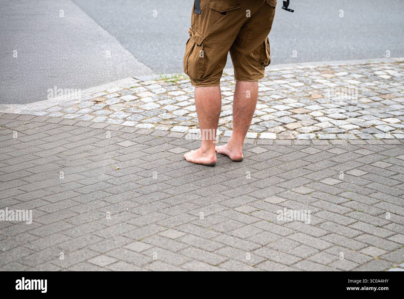 Uomo a piedi nudi in pantaloncini da carico in piedi su marciapiedi pavimentati e su strade acciottolate Foto Stock