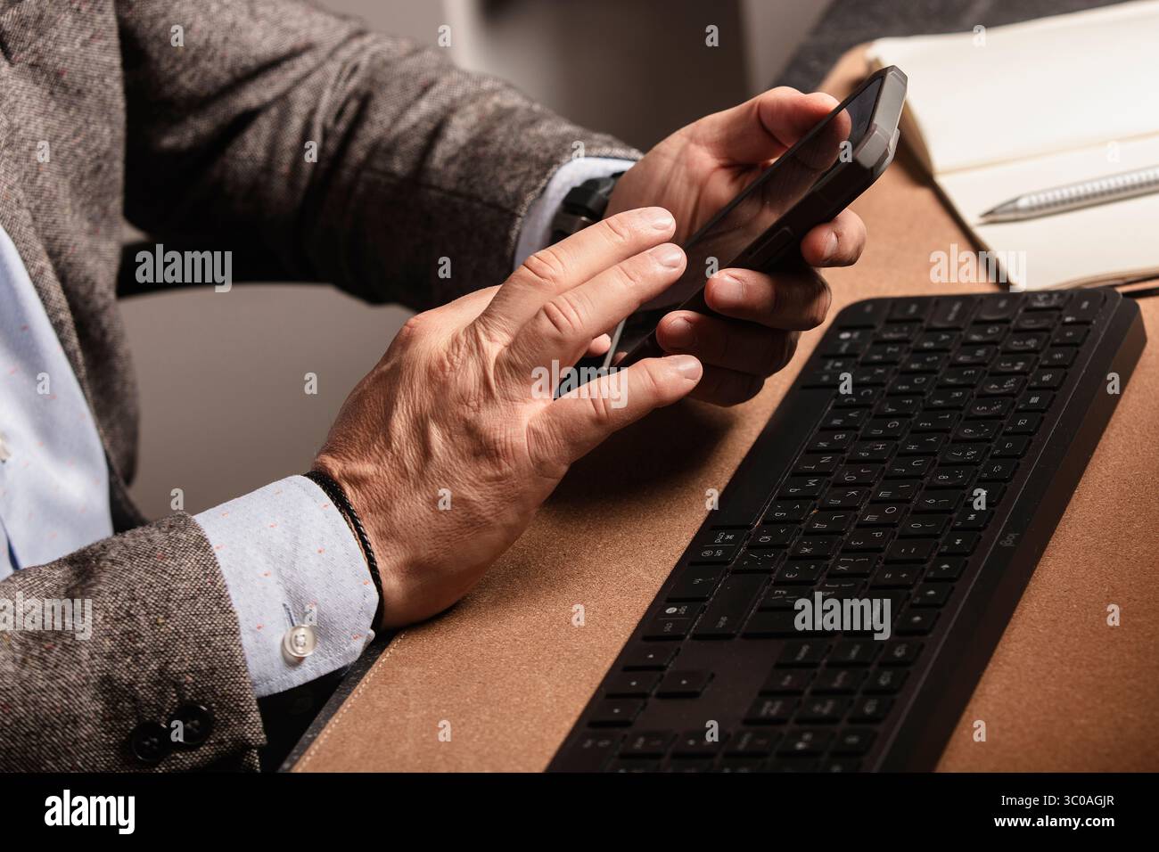 Uomo che utilizza lo smartphone alla moderna scrivania con tastiera, mouse, monitor e un bicchiere d'acqua. Area di lavoro minimalista, perfetta per lavorare in remoto Foto Stock