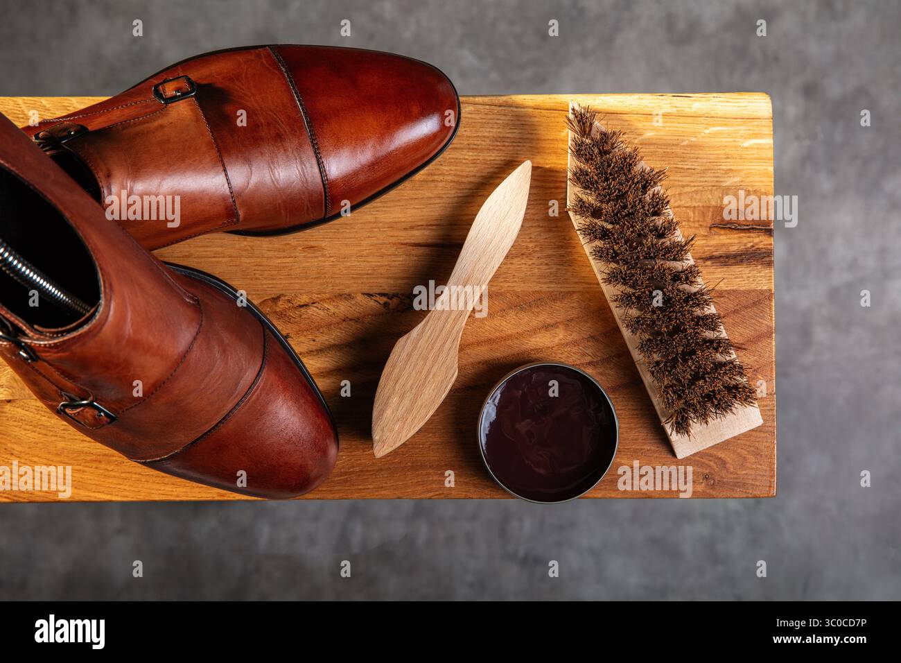 Vista dall'alto di un paio di scarpe in pelle marrone lucida posizionate accanto a una spazzola per scarpe in legno, un applicatore per lucidatura e uno stagno aperto di lucidatura marrone su una Foto Stock