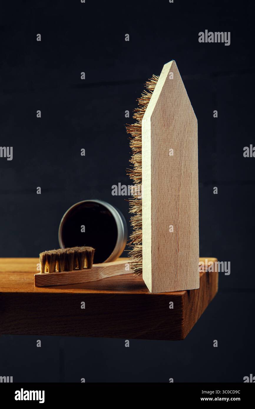 Immagine verticale con un primo piano di tradizionali spazzole per scarpe in legno e una scatola aperta di lucidatura scura su una superficie in legno. Un pennello è in posizione verticale Foto Stock
