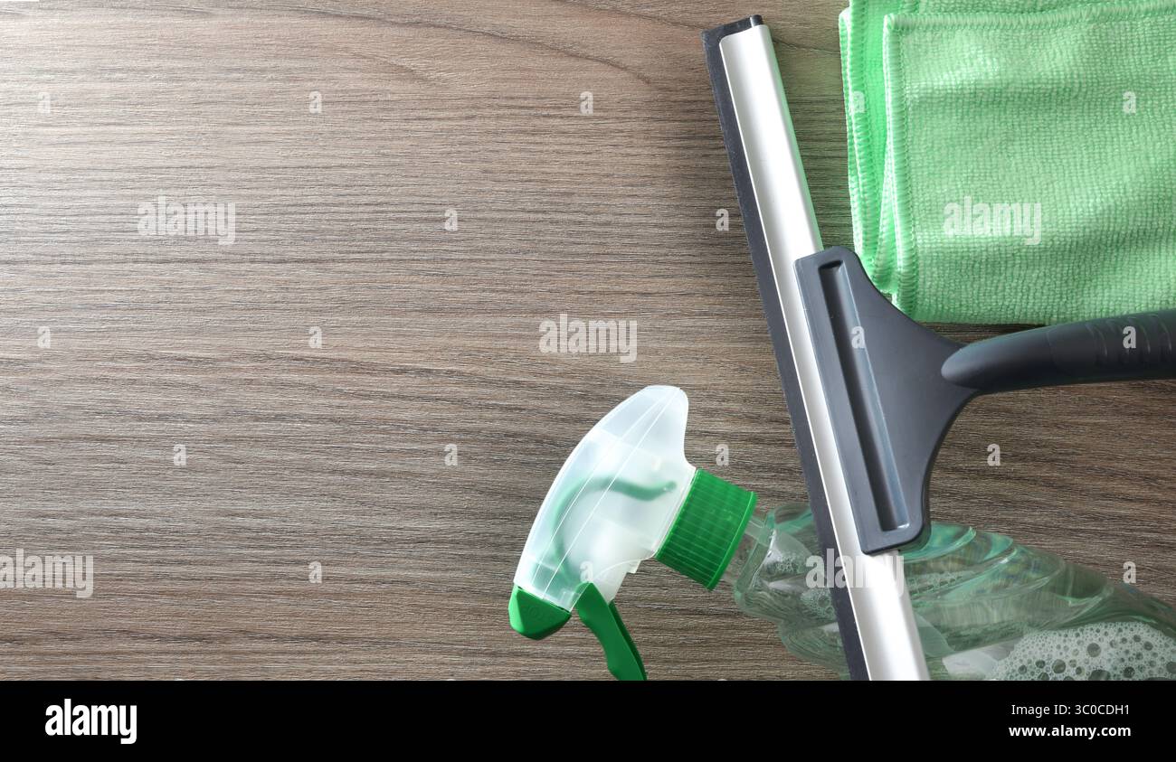Spatola detergente per vetri, prodotto spray e panno in microfibra isolato su un tavolo in legno. Vista dall'alto. Foto Stock
