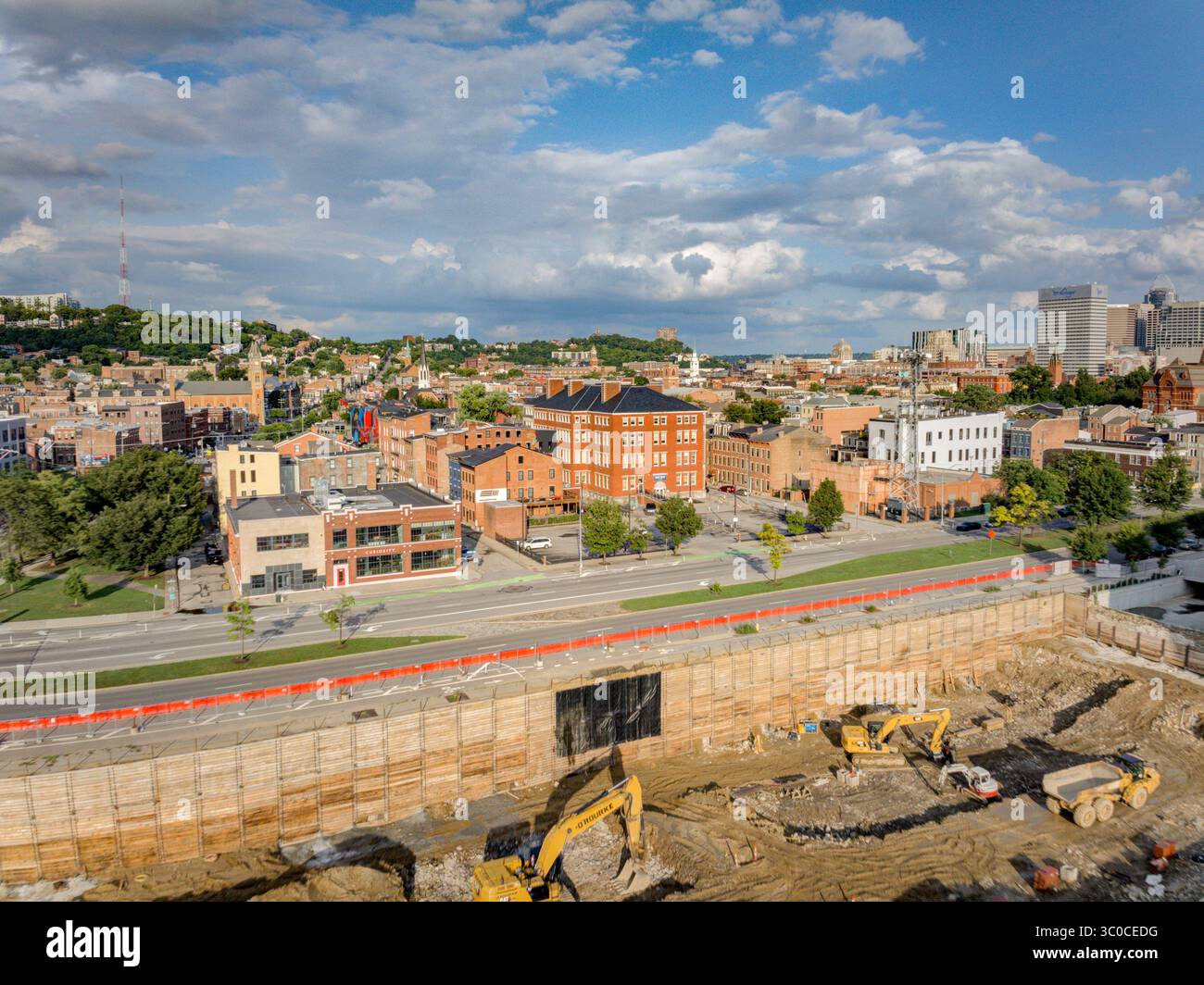 Cincinnati, Stati Uniti - 18 luglio 2025: Vista aerea di edifici in mattoni che gettano ombre, sito di scavo con macchinari gialli e un vivace skyline della città. Foto Stock