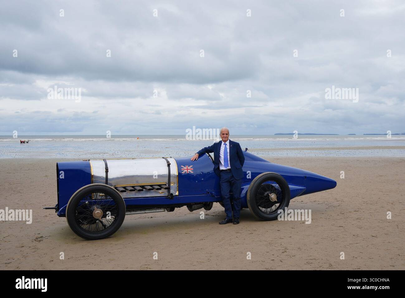 Don Wales, nipote di Sir Malcolm Campbell, con la Blue Bird Land Speed record car durante un evento centenario a Pendine Sands, Carmarthen, Galles del Sud. Il 21 luglio segna un secolo da quando Blue Bird ha fatto irruzione in Pendine Sands, stabilendo un nuovo record mondiale di velocità terrestre a 150 km/h (76 mph). Data foto: Lunedì 21 luglio 2025. Foto Stock