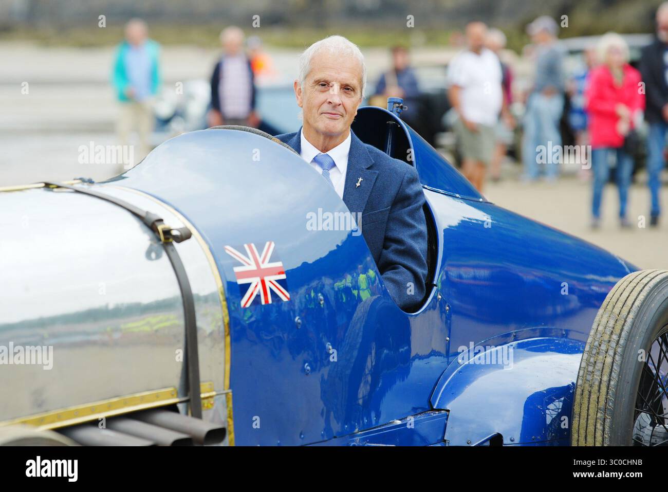 Don Wales, nipote di Sir Malcolm Campbell, con la Blue Bird Land Speed record car durante un evento centenario a Pendine Sands, Carmarthen, Galles del Sud. Il 21 luglio segna un secolo da quando Blue Bird ha fatto irruzione in Pendine Sands, stabilendo un nuovo record mondiale di velocità terrestre a 150 km/h (76 mph). Data foto: Lunedì 21 luglio 2025. Foto Stock