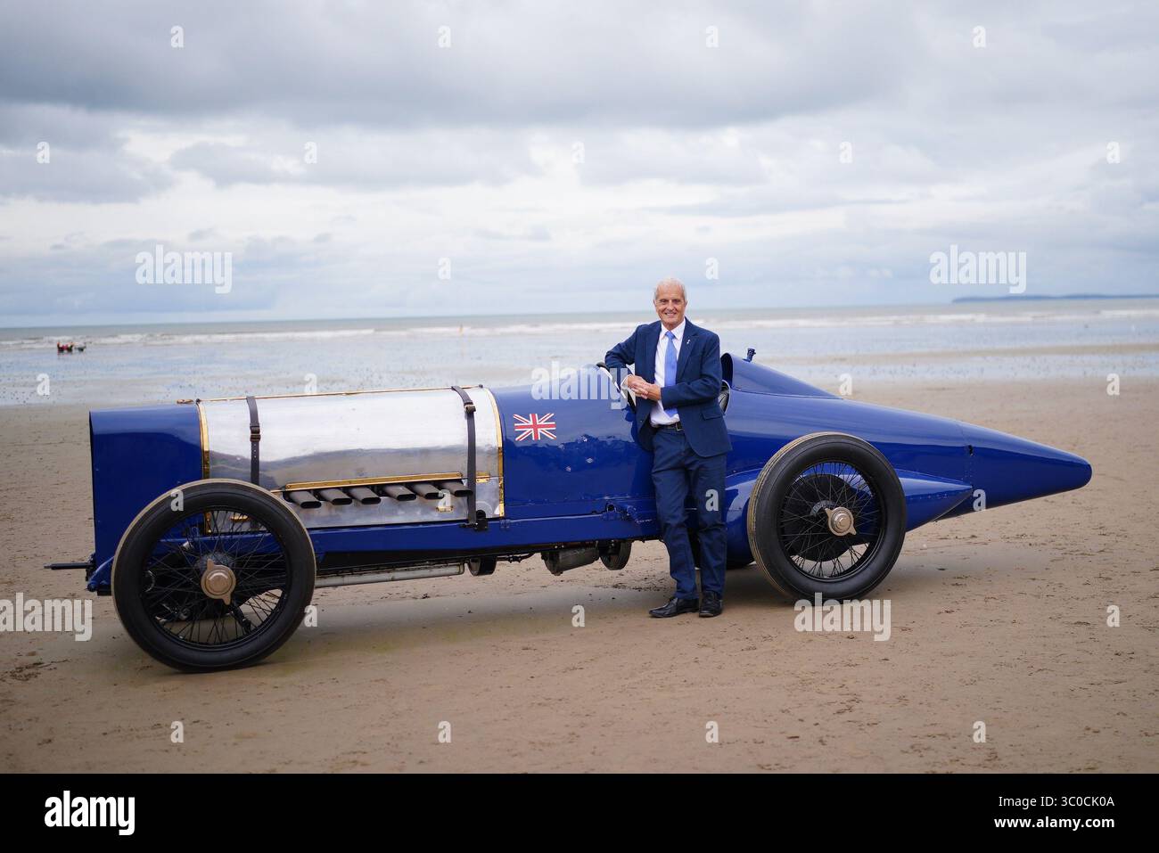 Don Wales, nipote di Sir Malcolm Campbell, con la Blue Bird Land Speed record car durante un evento centenario a Pendine Sands, Carmarthen, Galles del Sud. Il 21 luglio segna un secolo da quando Blue Bird ha fatto irruzione in Pendine Sands, stabilendo un nuovo record mondiale di velocità terrestre a 150 km/h (76 mph). Data foto: Lunedì 21 luglio 2025. Foto Stock