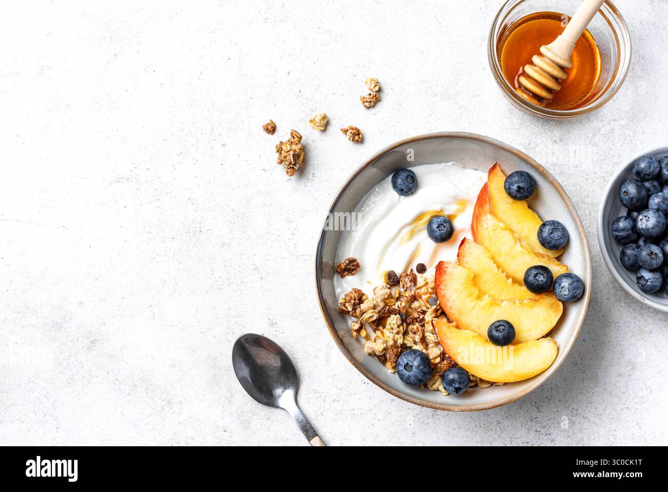 Ciotola di muesli per una sana colazione su sfondo bianco, vista dall'alto, spazio per fotocopie. Muesli fatti in casa con yogurt greco, pesche e mirtilli. Mangiare sano Foto Stock
