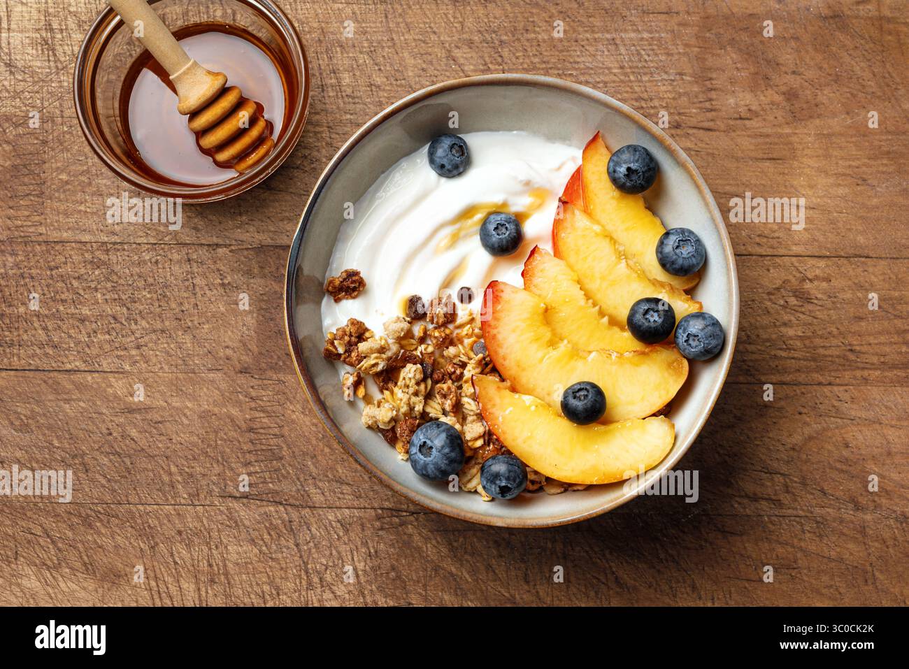 Ciotola di muesli per una sana colazione su sfondo di legno, vista dall'alto. Muesli fatti in casa con yogurt greco, pesche e mirtilli. Mangiare sano, stagione Foto Stock