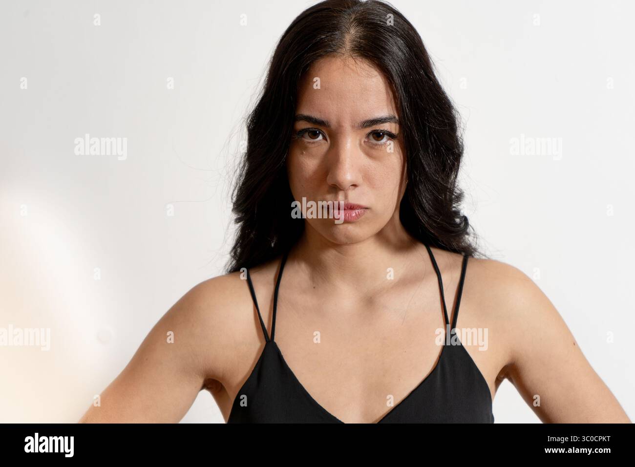 Ritratto di una giovane donna con lunghi capelli scuri che crea un viso infastidito ed esprime emozioni negative Foto Stock