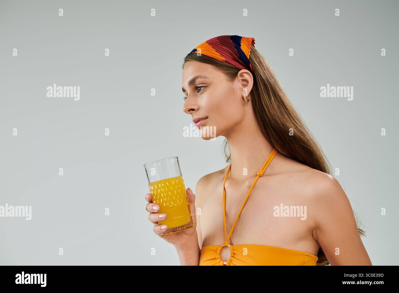 Una giovane donna con la pelle abbronzata posa con sicurezza in un vivace abito estivo, bevi in mano. Foto Stock
