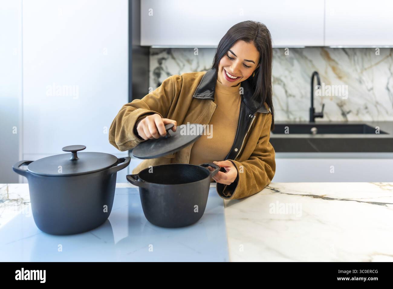 Donna sorridente che sceglie una pentola da cucina in un luminoso reparto di utensili da cucina di un negozio di articoli per la casa, godendo della varietà di opzioni disponibili Foto Stock