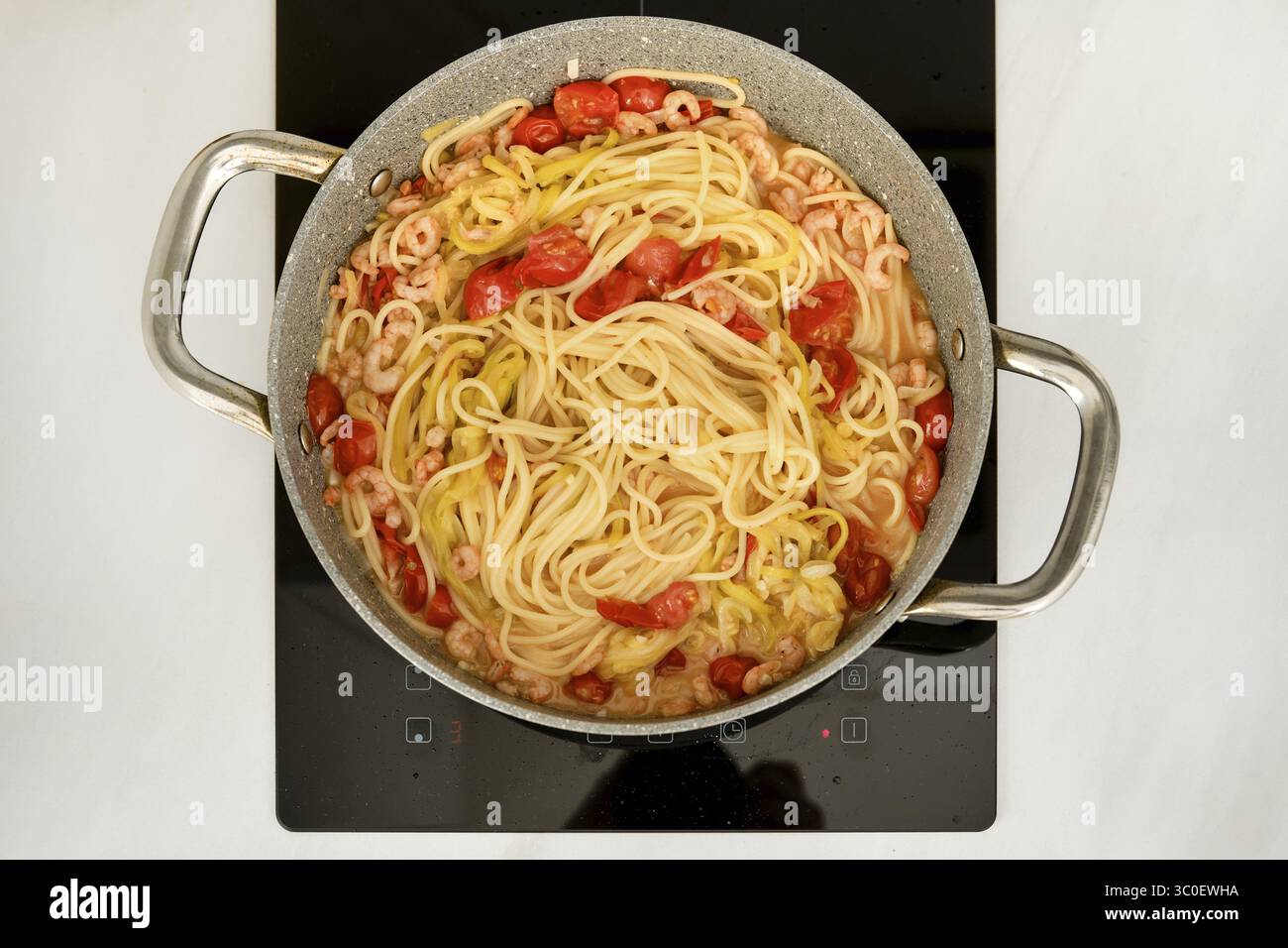 Una pentola di spaghetti sta bollendo su una stufa, mescolata con gamberi e pomodori ciliegini Foto Stock