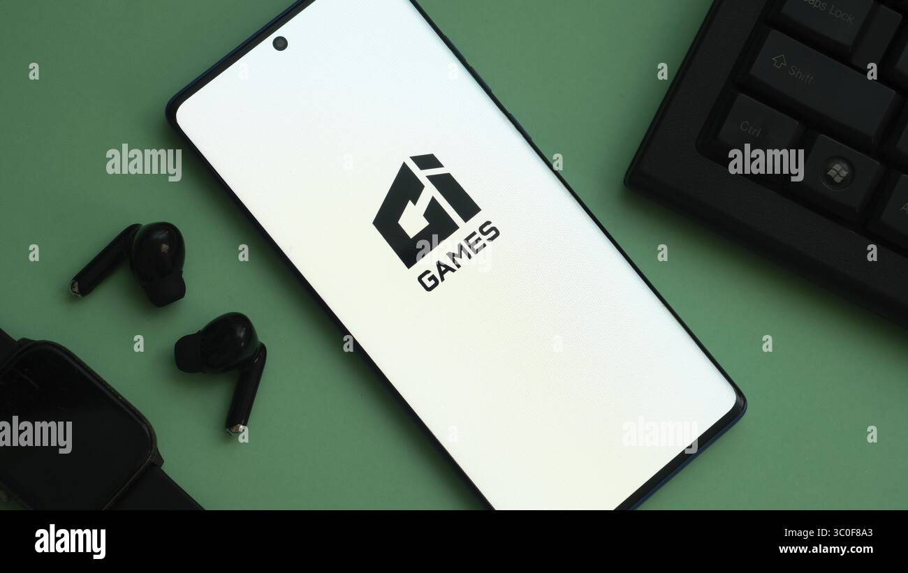 Smartphone con logo "gi GAMES" su superficie verde con accessori Foto Stock
