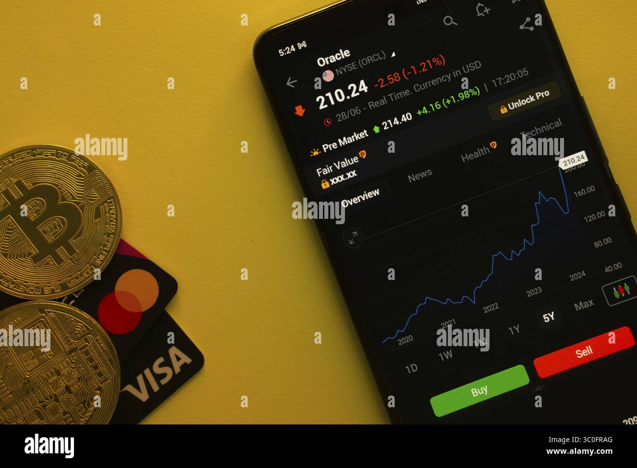 Dhaka, Bangladesh - 30 giugno 2025: Smartphone che visualizza i dati azionari Oracle su un'app di trading con Bitcoin, Visa e Mastercard su una vivace b gialla Foto Stock