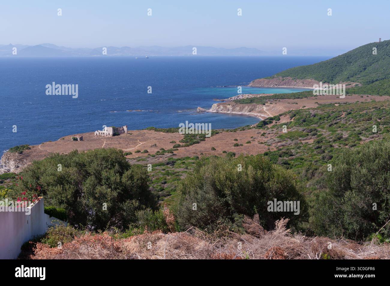 Tranquillo paesaggio costiero che mostra lo stretto di gibilterra, caratterizzato da un edificio abbandonato, vegetazione secca e vegetazione lussureggiante, che mette in risalto il Be Foto Stock