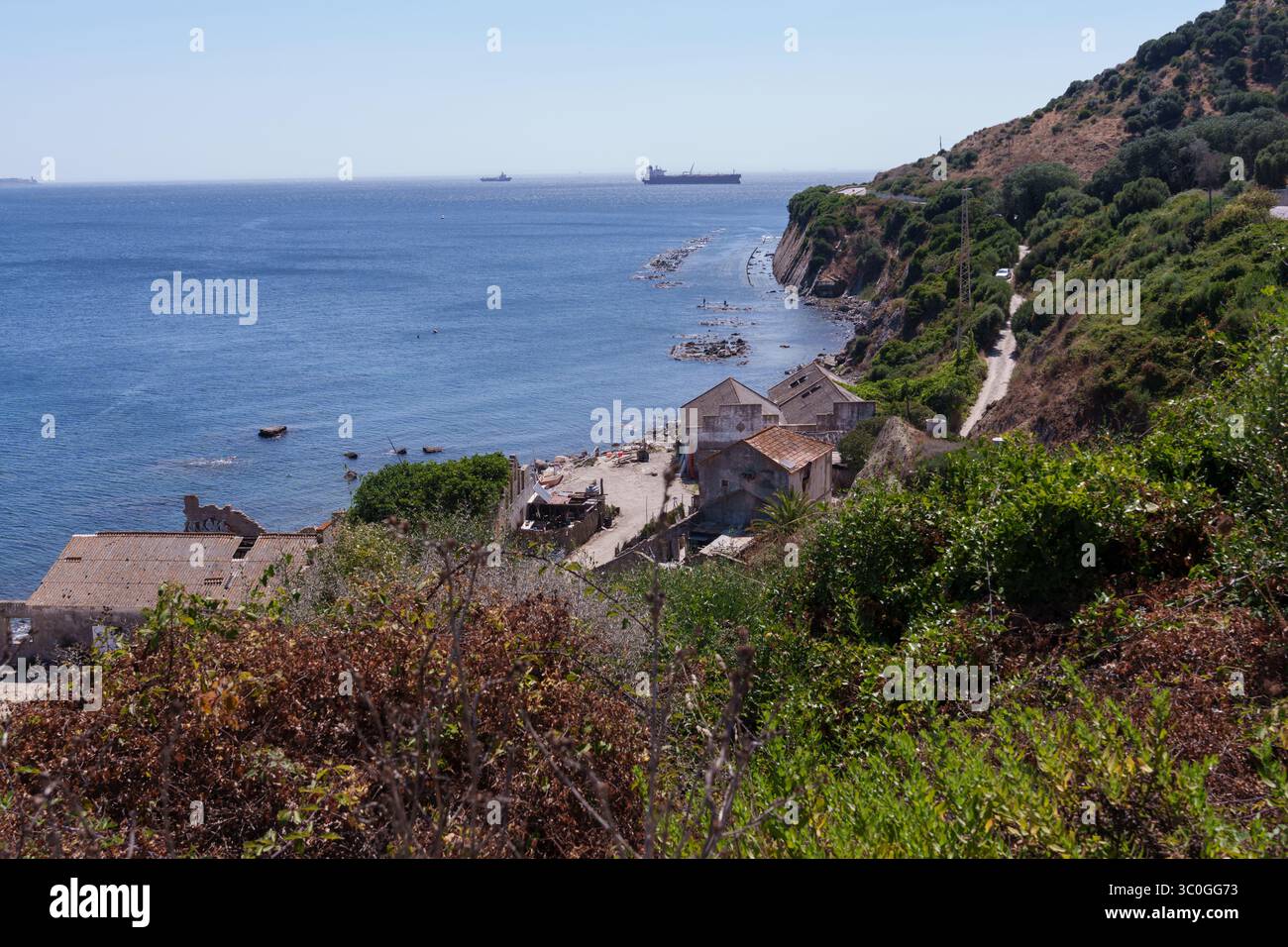 Navi da carico che attraversano lo stretto di gibilterra, rivelando un insediamento minerario costiero abbandonato contro la costa rocciosa del mediterraneo Foto Stock