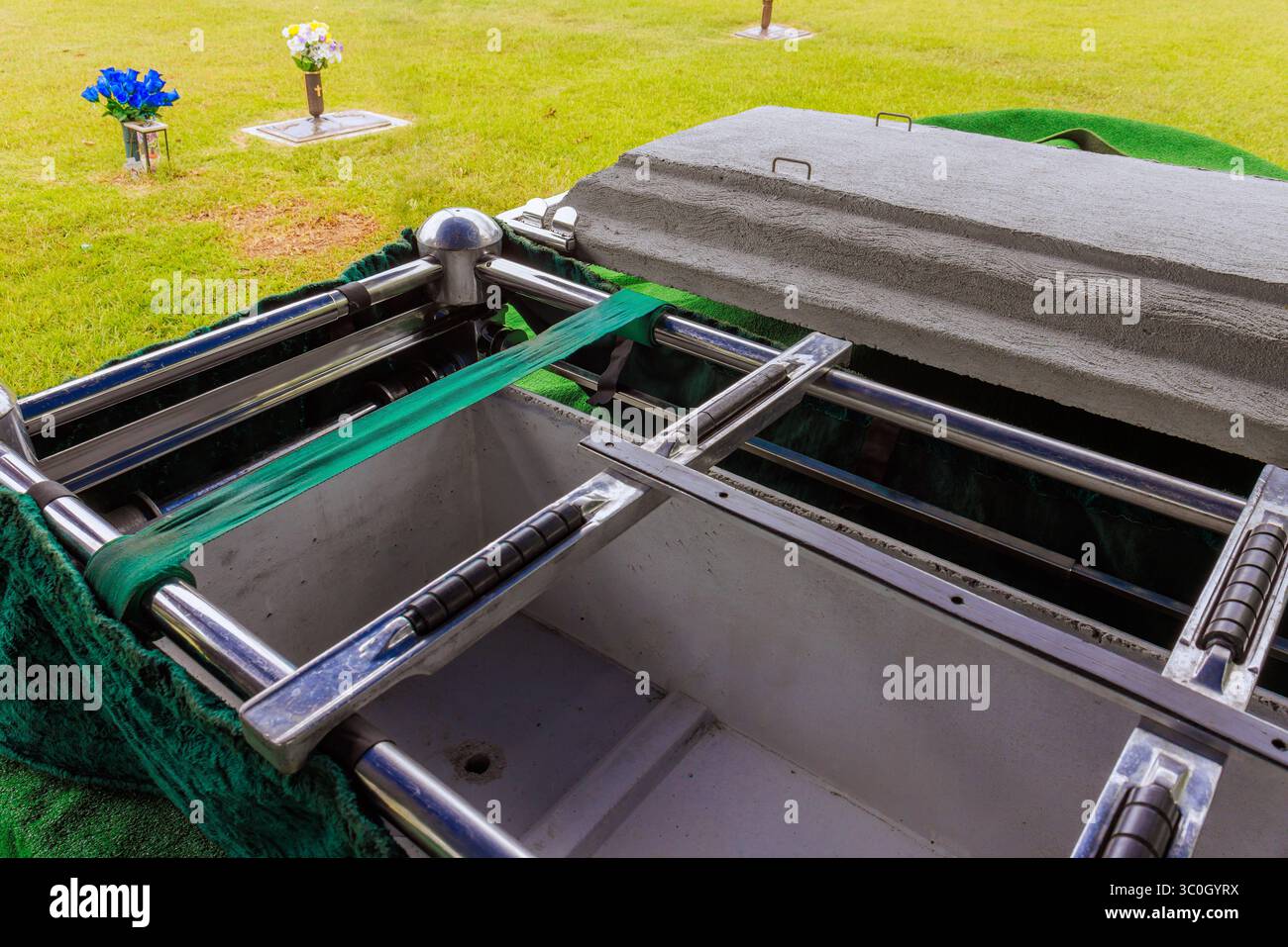 La bara è in fase di preparazione presso il cimitero con fiori collocati nelle vicinanze durante la cerimonia solenne diurna. Foto Stock