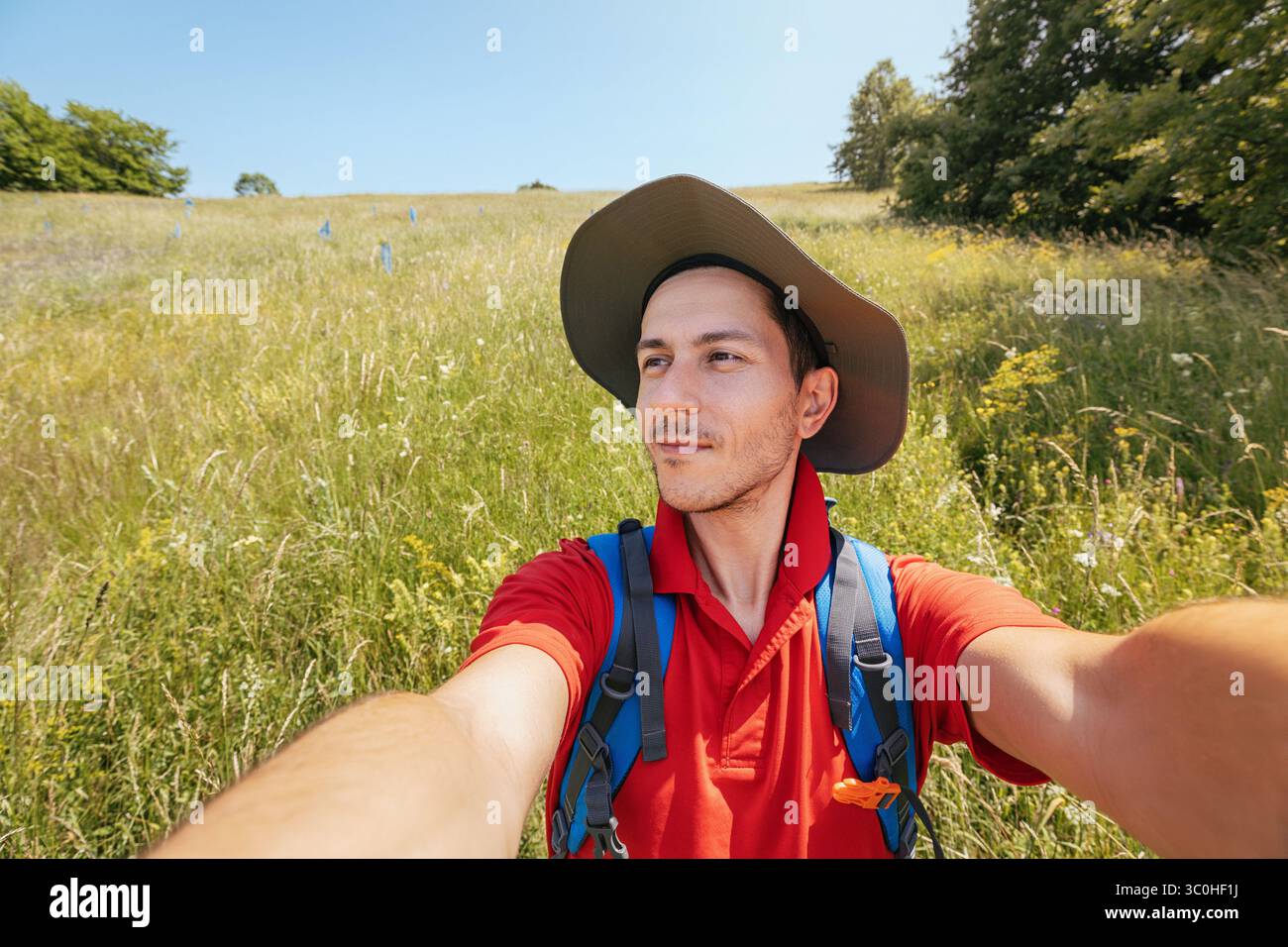 Biologo che indossa un cappello e uno zaino che scatta un selfie con il suo telefono in un campo durante la ricerca biologica Foto Stock