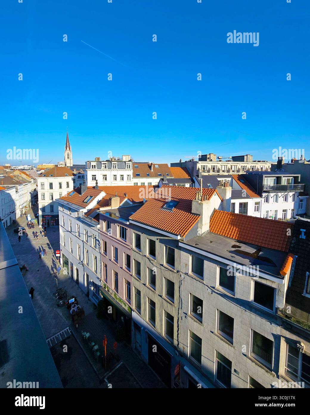 Vista diurna elevata sui tetti di Bruxelles con una guglia della chiesa e un cielo azzurro luminoso sullo sfondo. - Immagine stock catturata con smartphone