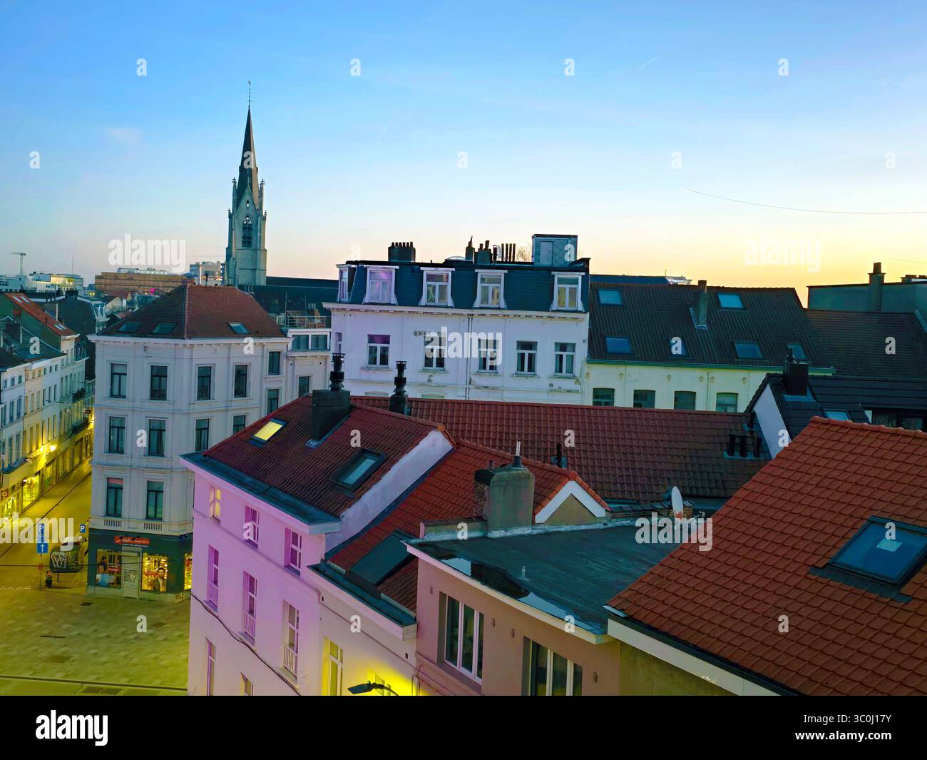 Vista all'alba sul tetto di Bruxelles, caratterizzata da una guglia della chiesa e da edifici dal tetto rosso sotto un cielo tenue e sfumato. Foto Stock