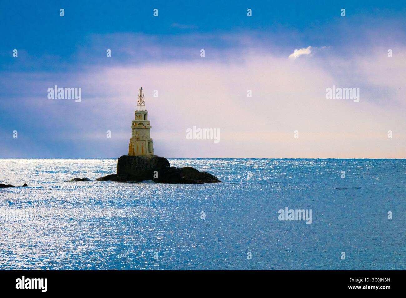 Un alto faro sovrasta un'isola rocciosa, circondata da calme acque oceaniche. La scena cattura un bellissimo cielo del tardo pomeriggio, con luce soffusa Foto Stock