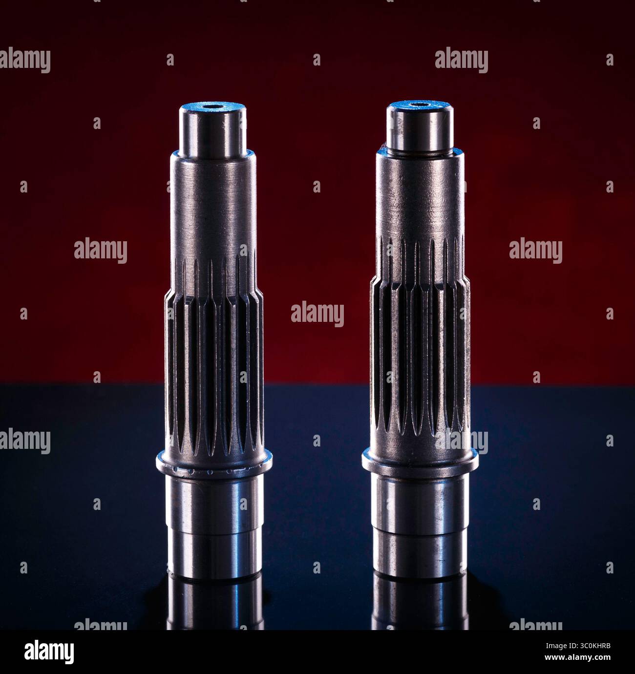 Due alberi cilindrici in metallo sono presentati su uno sfondo rosso scuro. Gli alberi sono realizzati in metallo grigio scuro, probabilmente acciaio o ferro, e sono dotati di Foto Stock