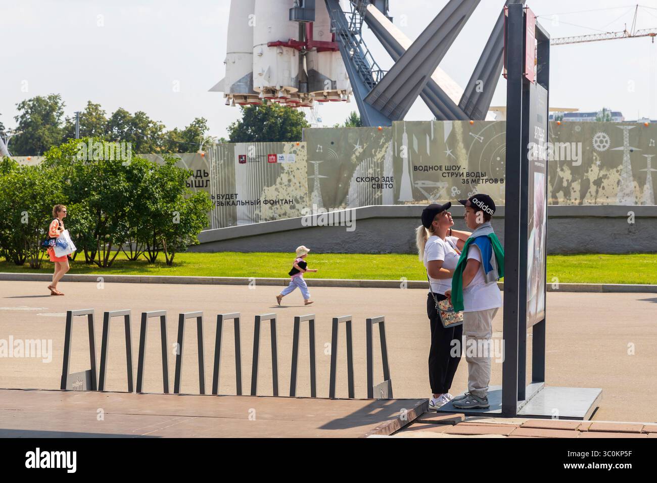Mosca, Russia – 15 maggio 2025: Spazio all'aperto con mostra di razzi al VDNKh: Visitatori e portabiciclette in primo piano Foto Stock