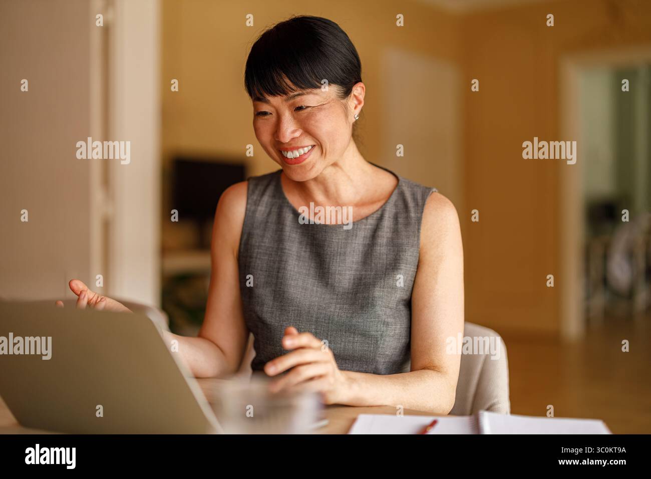 Donna d'affari di medie dimensioni sorridente e impegnata nella pianificazione di progetti in videoconferenza tramite laptop nell'ufficio aziendale Foto Stock