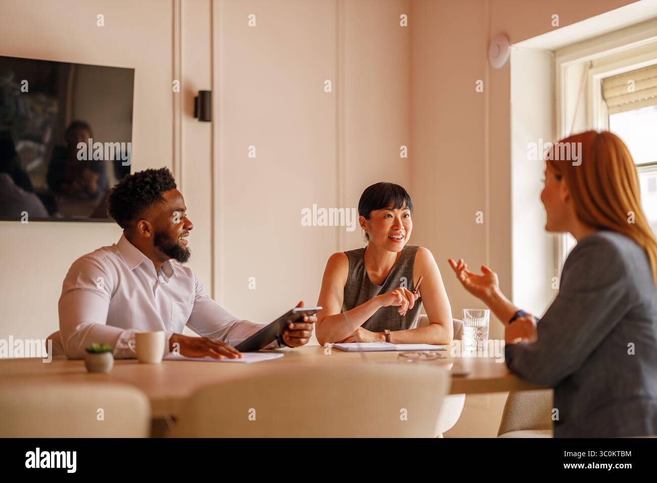 Gruppo felice di colleghi che lavorano insieme a progetti in sala riunioni utilizzando computer e documenti Foto Stock