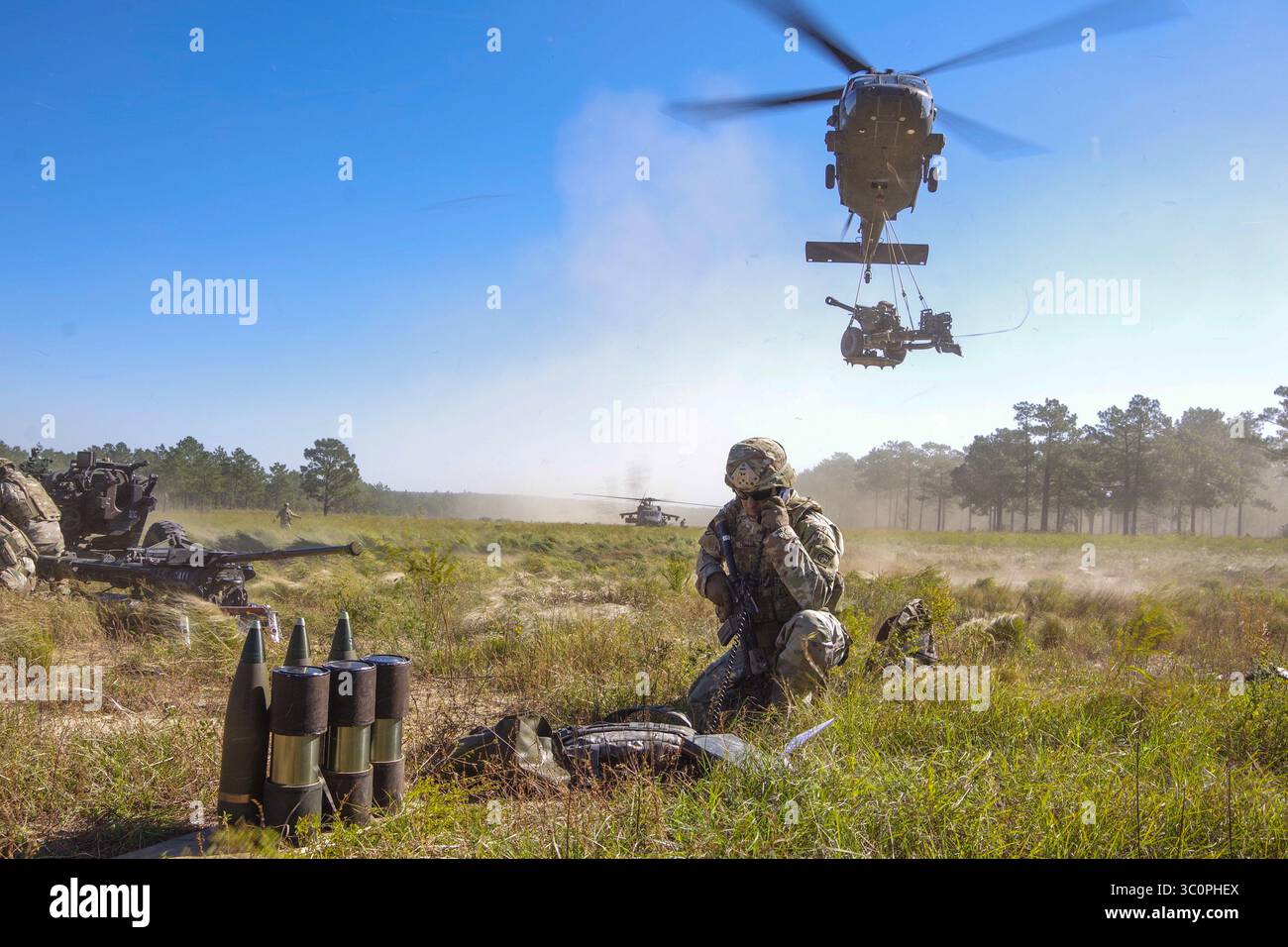 24 ottobre 2018 - Fort Bragg, Carolina del Nord, Stati Uniti - Un elicottero UH-60 Blackhawk pilotato da aviatori della compagnia C, 2-82 Aviation Regiment, 82nd Combat Aviation Brigade sling-loads un M119A3 Howitzer appartenente alla Alpha Battery, 1st Battalion, 319th Airborne Field Artillery Regiment, 3rd Brigade Combat Team, 82nd Airborne Division mentre un paracadutista della batteria riceve i dettagli della missione 2018 sul fuoco radio del North Carolina Oct. L'operazione ha testato le capacità dei paracadutisti e degli aviatori per integrare le loro capacità W Foto Stock