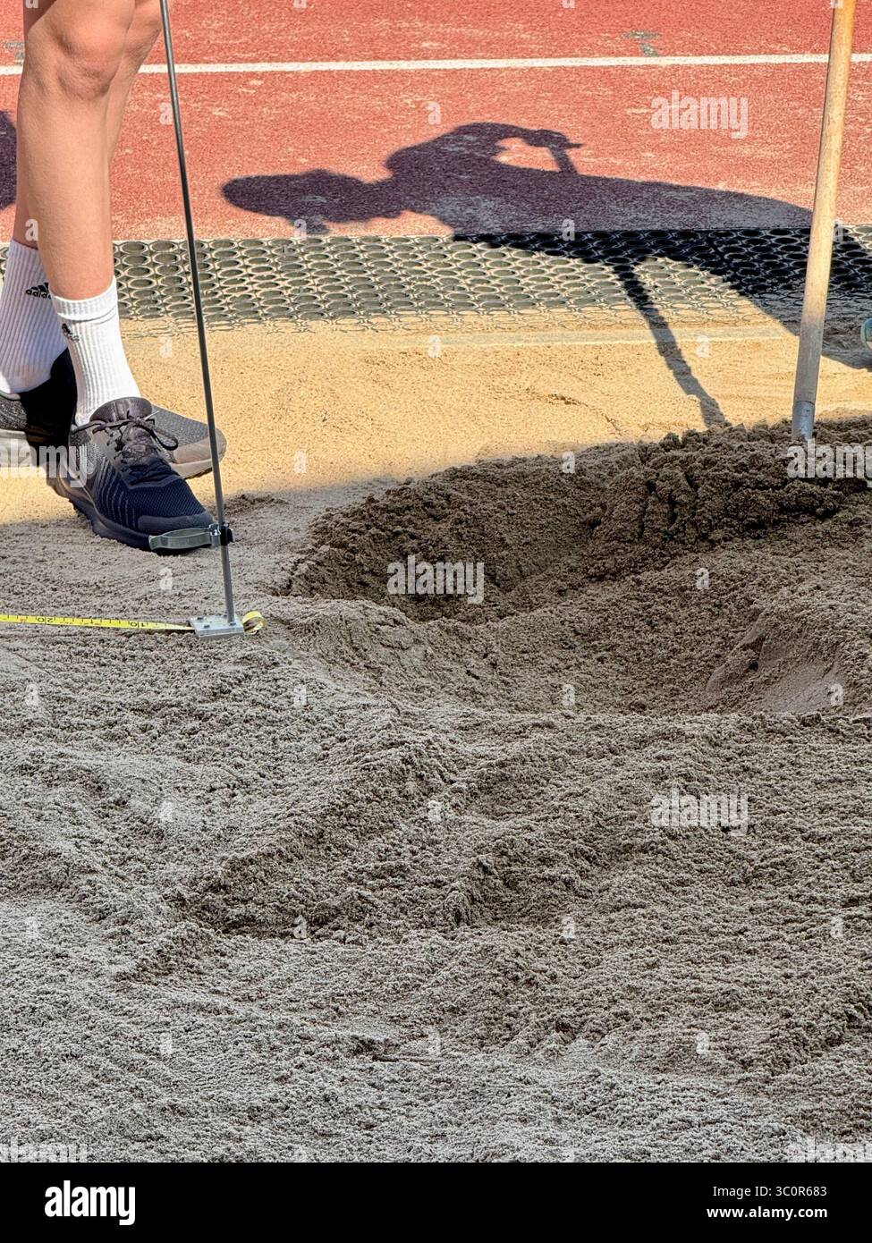 Salto lungo atterrando nella fossa di sabbia durante una gara di atletica leggera, misurazione della distanza di salto con nastro adesivo. Foto Stock