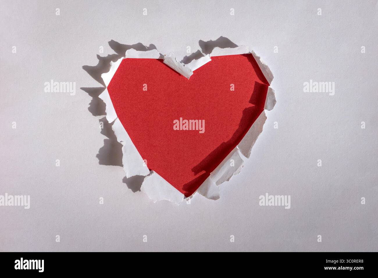 Foro rosso a forma di cuore strappato attraverso carta bianca. Copia spazio. Foto Stock