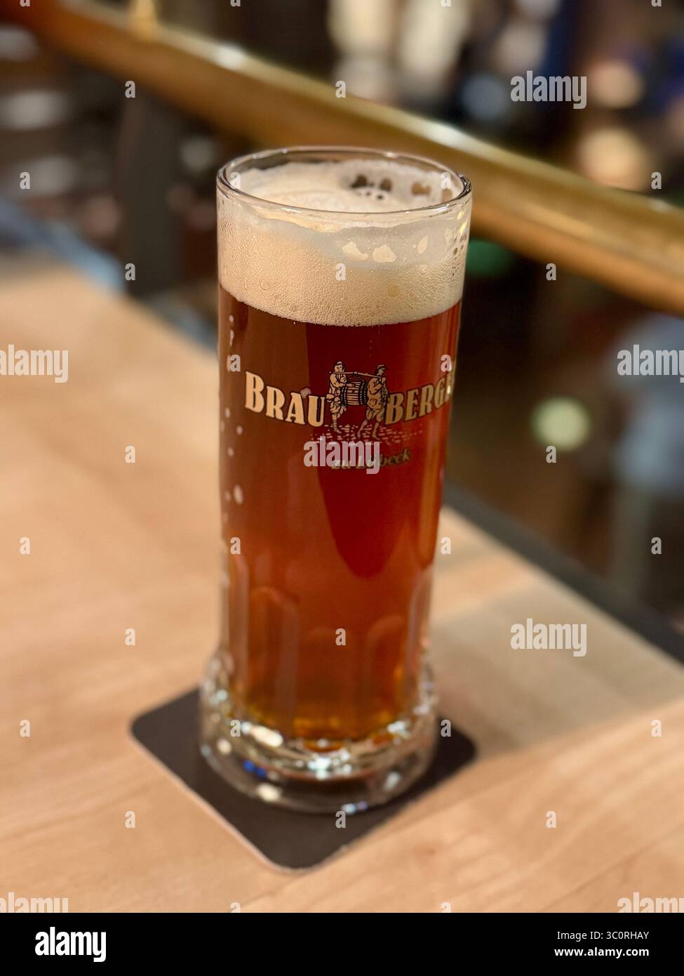 Primo piano di un alto bicchiere di birra ambrata con schiuma sopra, servito in un bar in Germania. - Immagine stock catturata con smartphone