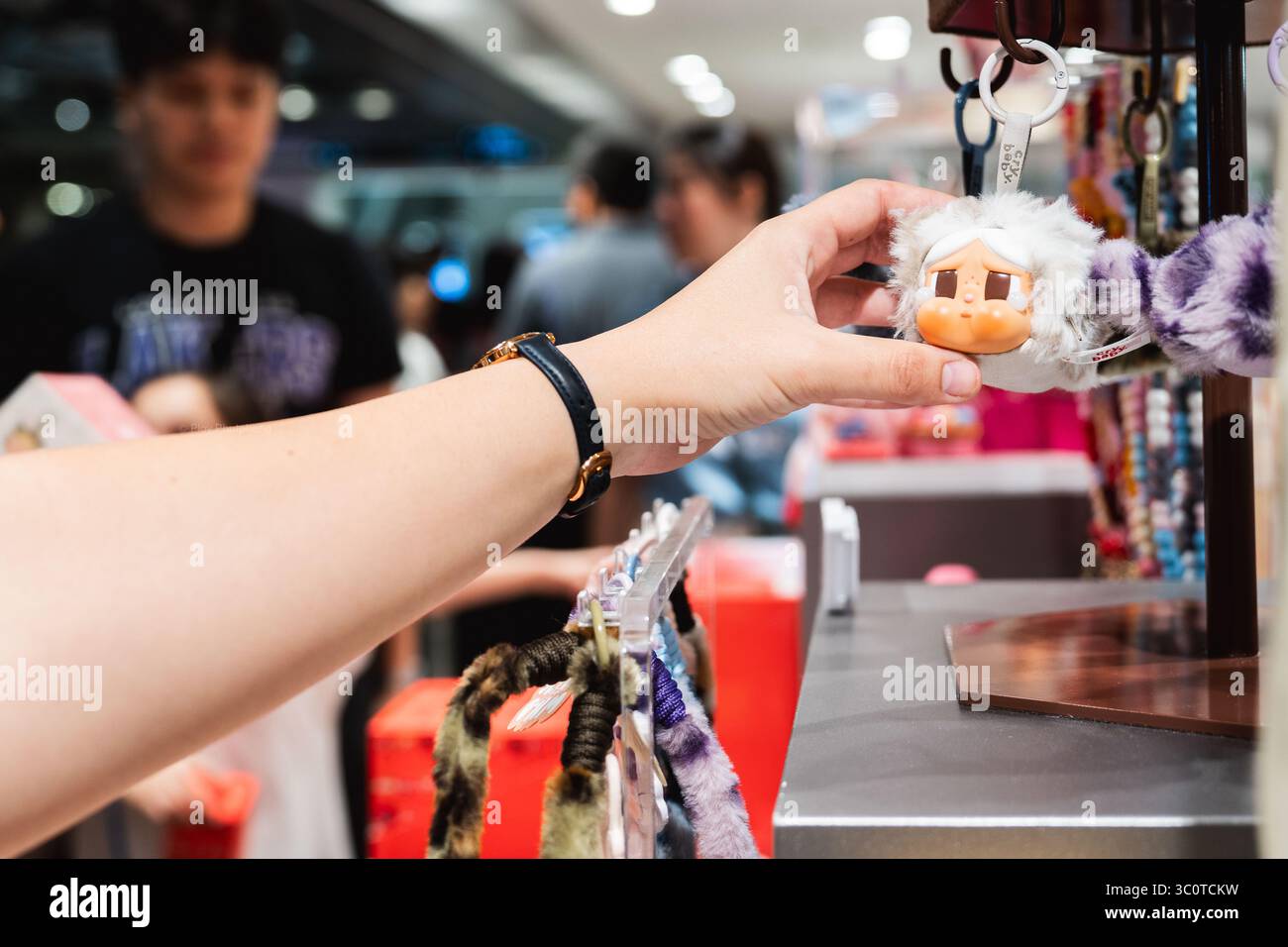 Un cliente regge un portachiavi con un personaggio da collezionare all'interno di un affollato negozio Pop Mart. I collezionisti di scatole cieche di POP Mart hanno scatenato una mania culturale in tutta l'Asia e oltre, con i fan che inseguono figure rare come Labubu e Molly. Lanciato nel 2016 con le bambole Molly dall'artista di Hong Kong Kenny Wong, il marchio ha riscosso un enorme successo grazie alle vendite guidate dalla suspense. Attualmente presente in oltre 30 paesi e raggiungendo quasi 100 attraverso pop-up e partnership, Pop Mart ha trasformato i giocattoli di design in un fenomeno globale. Foto Stock
