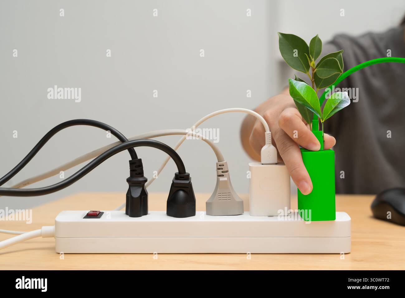 Collegare manualmente un dispositivo verde con foglie in una presa multipla piena di cavi, che simboleggia l'energia verde, l'energia pulita, il risparmio energetico e la CA ambientale Foto Stock