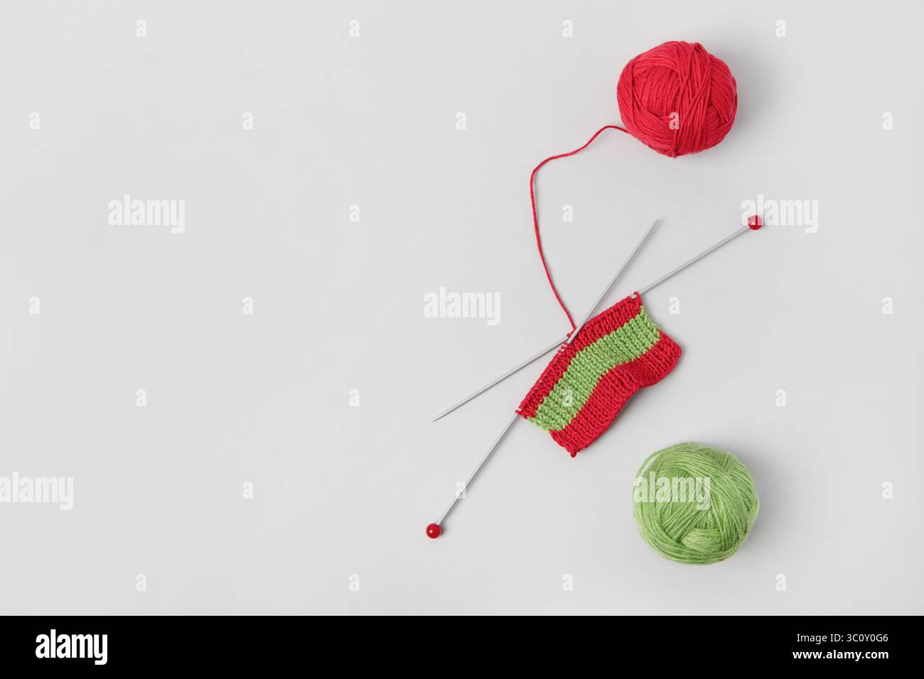 Lana a maglia rossa su sfondo grigio con aghi per maglieria per abiti caldi e hobby. Maglia una sciarpa natalizia a righe con re Foto Stock