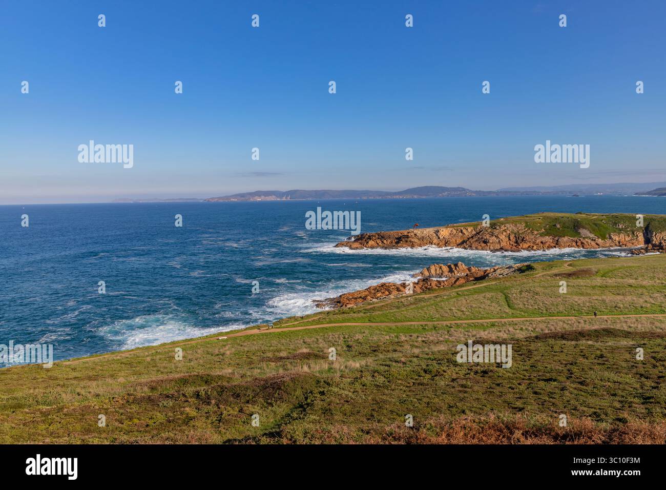 Paesaggio costiero in Una Coruna con scogliere rocciose, onde che si infrangono contro di loro e un cielo azzurro. Foto Stock